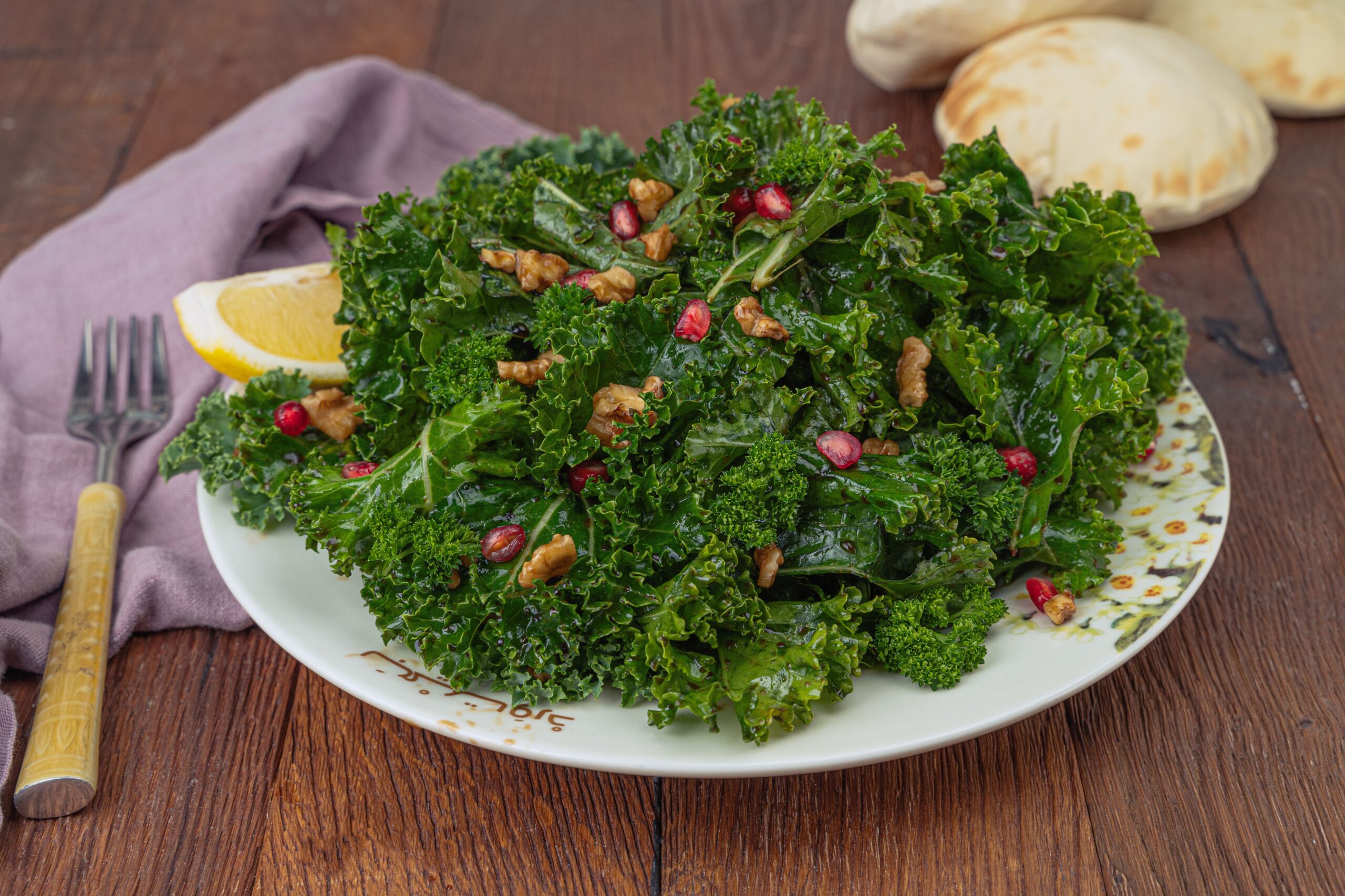 A fresh kale salad topped with walnuts and pomegranate seeds, served with lemon