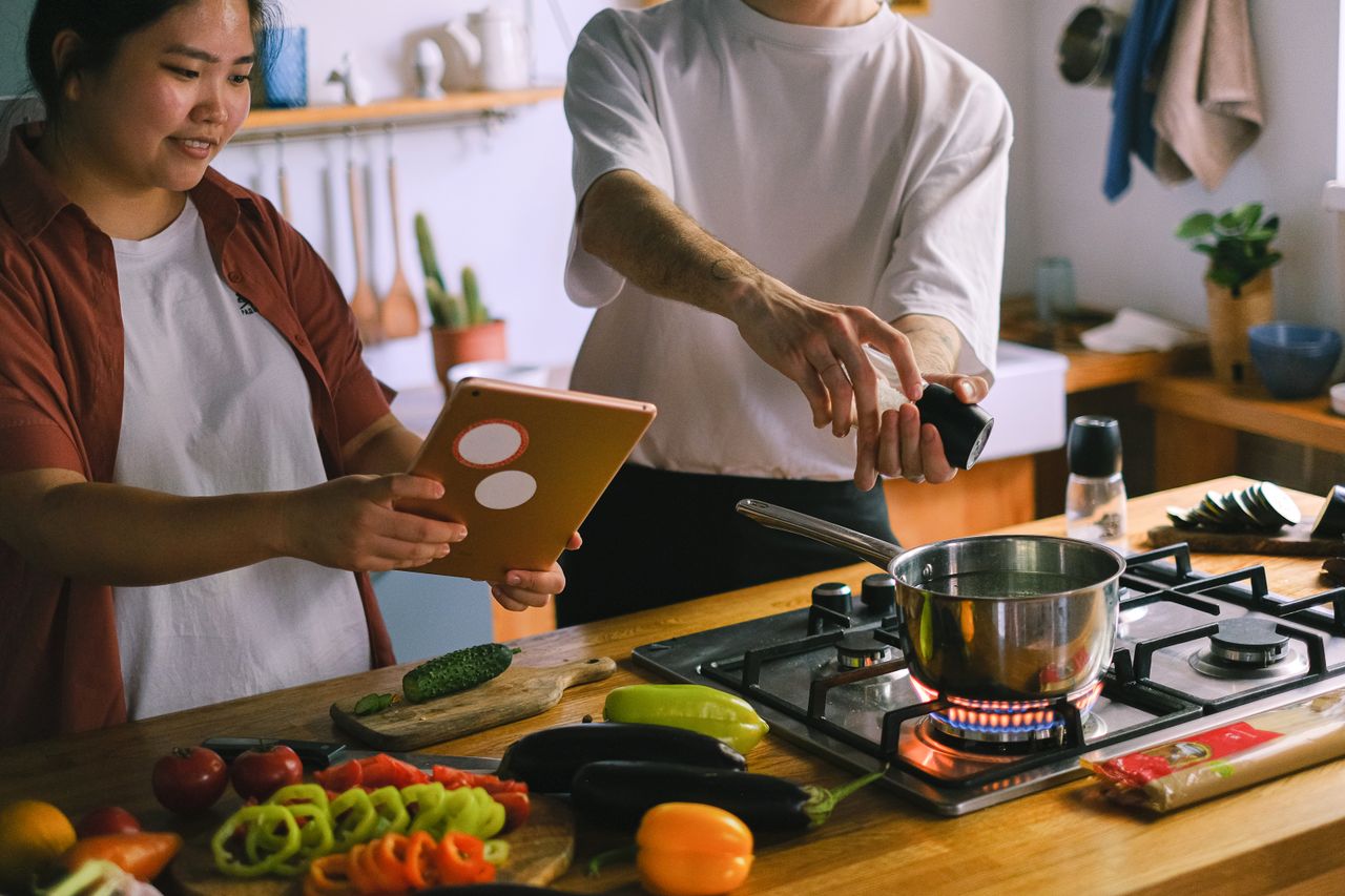 contact-img A happy couple using a tablet while preparing a meal in a stylish kitchen.