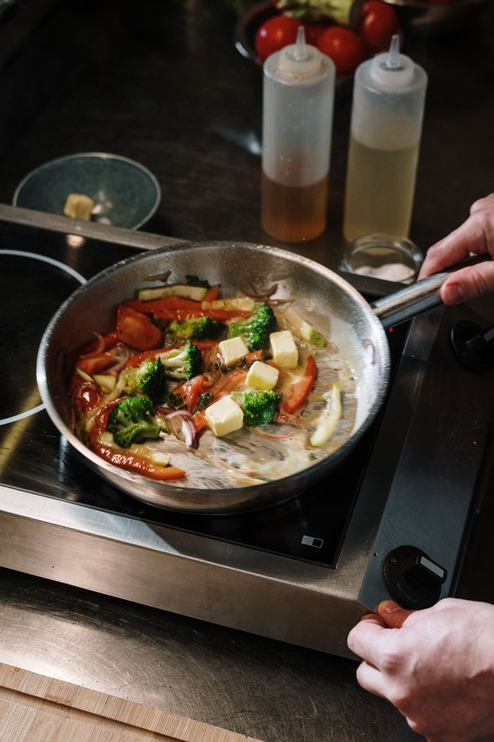 services-02 A chef cooks colorful vegetables in a skillet with butter on a stove in the kitchen.