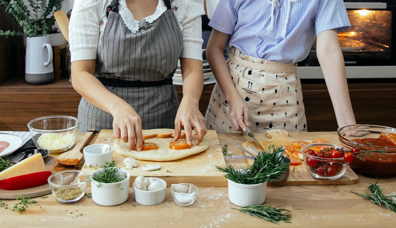 gallery-5 Crop unrecognizable females in aprons cooking pizza with tomatoes and cheese in kitchen together