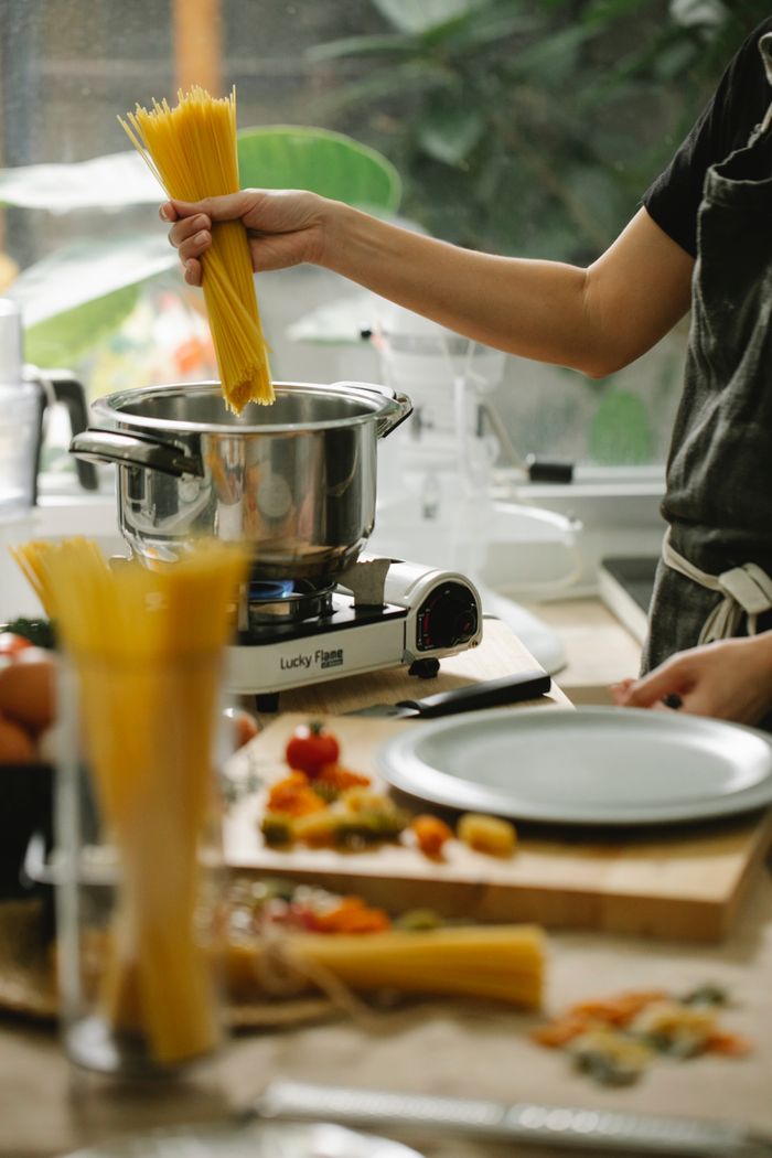 gallery-2 Crop unrecognizable female chef in apron putting raw spaghetti into saucepan on stove while cooking in contemporary light kitchen