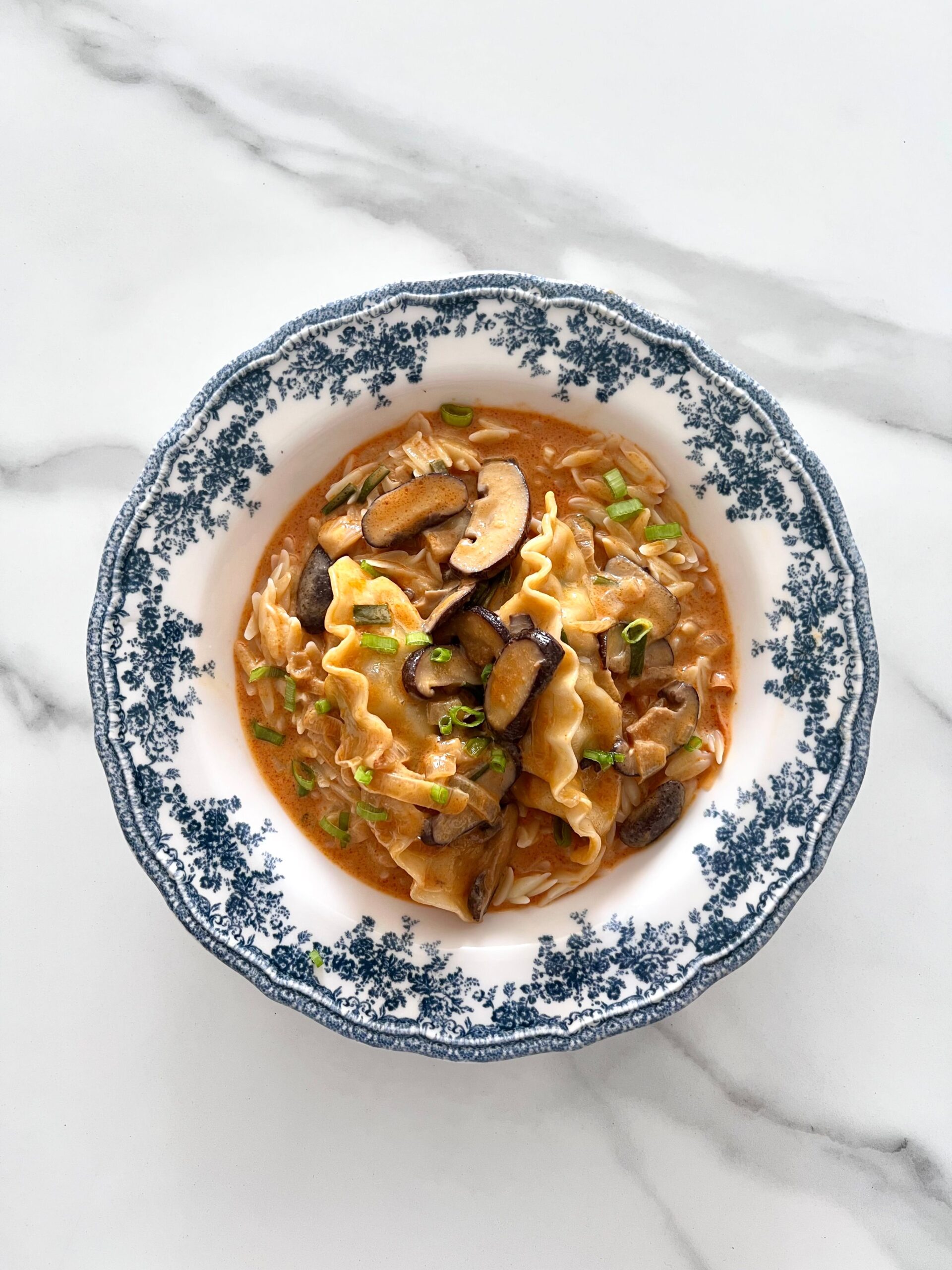 Top view of shiitake mushroom pasta in blue floral dish on marble surface.
